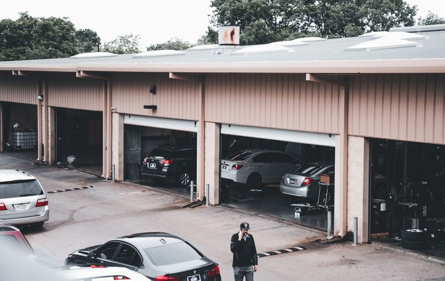 A man walks by a garage with cars parked inside and outside in an urban setting
